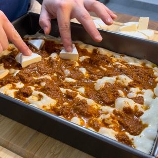 Una persona sta mettendo dei pezzi di formaggio sopra una padella di cibo