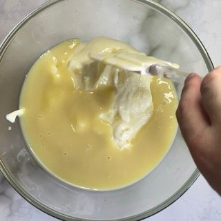 Una persona sta mescolando un liquido giallo in una ciotola di vetro con una spatola.