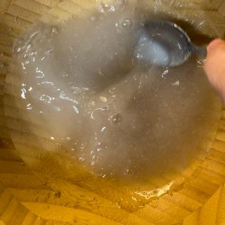 Una persona tiene in mano un cucchiaio in una ciotola piena di liquido.