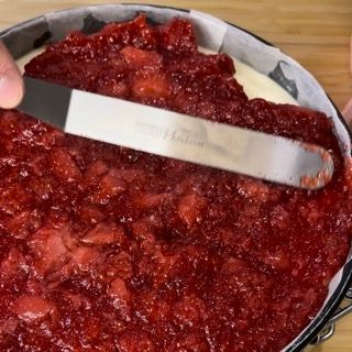 Una persona sta spalmando la salsa di fragole su una torta con una spatola