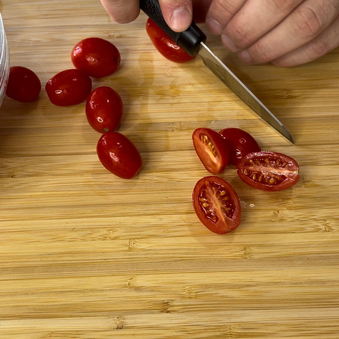 Una persona sta tagliando i pomodori su un tagliere di legno