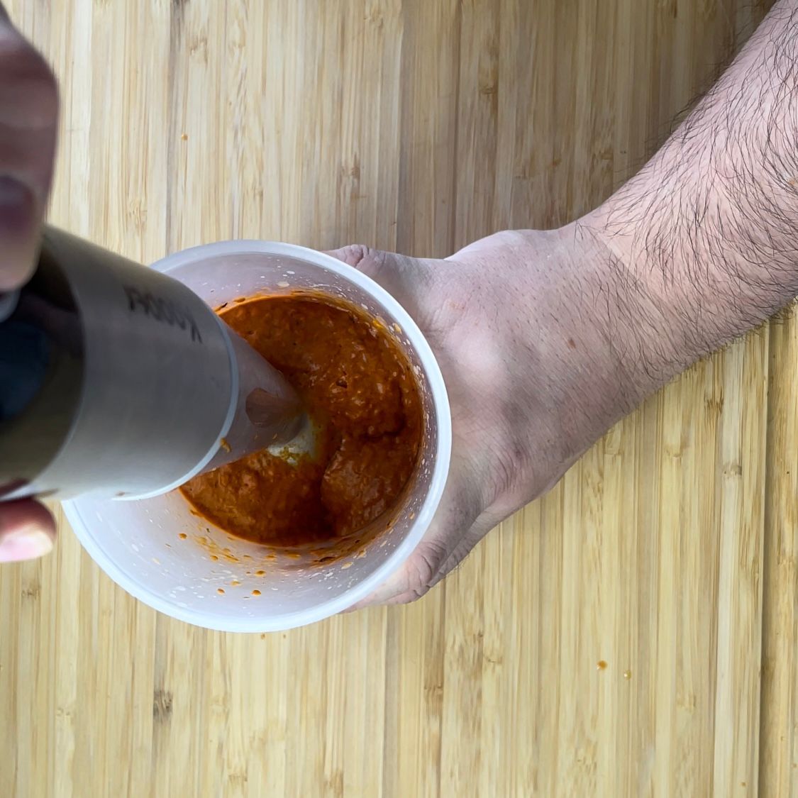 Una persona sta mescolando una salsa in una tazza con un frullatore.