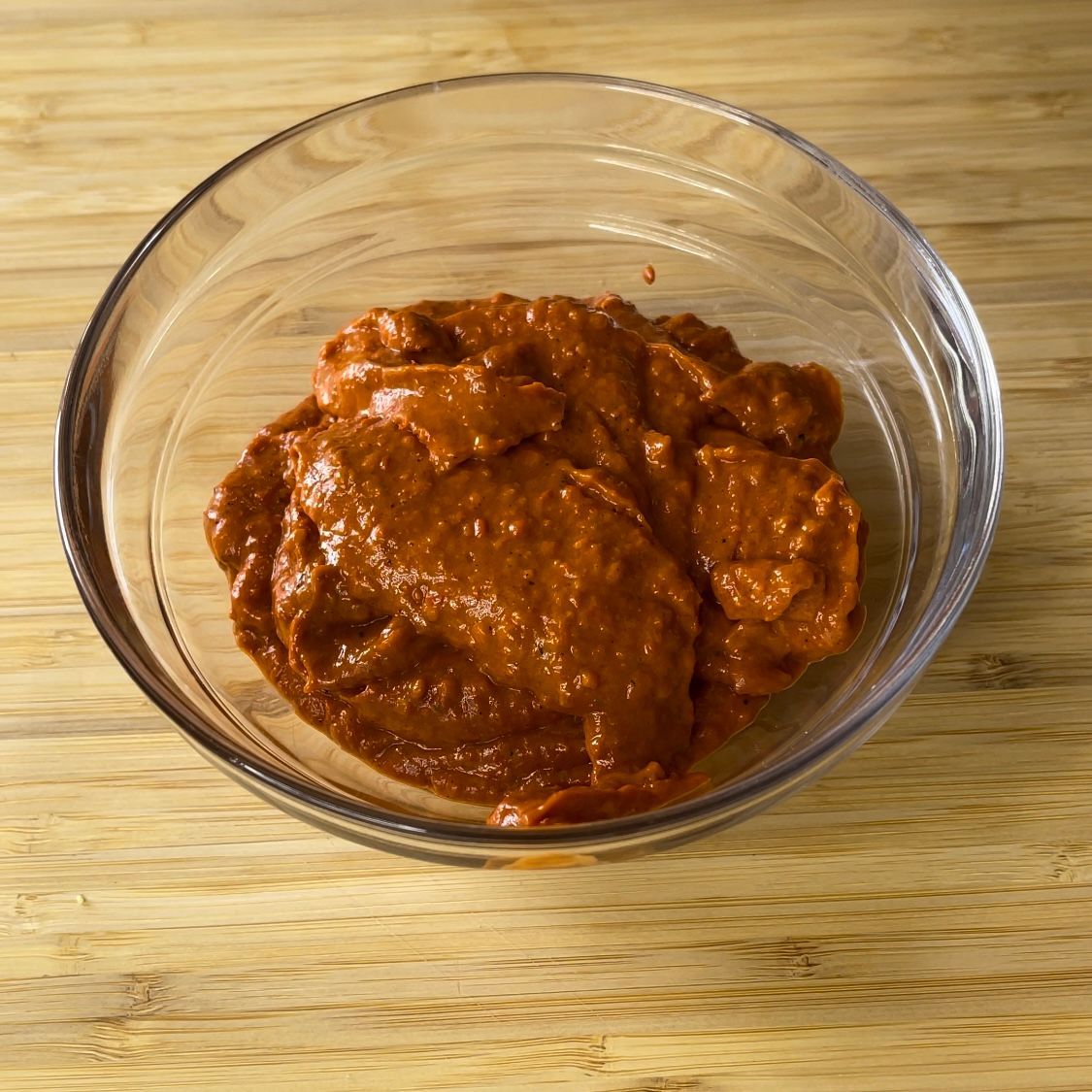 Una ciotola di vetro piena di salsa rossa su un tavolo di legno.