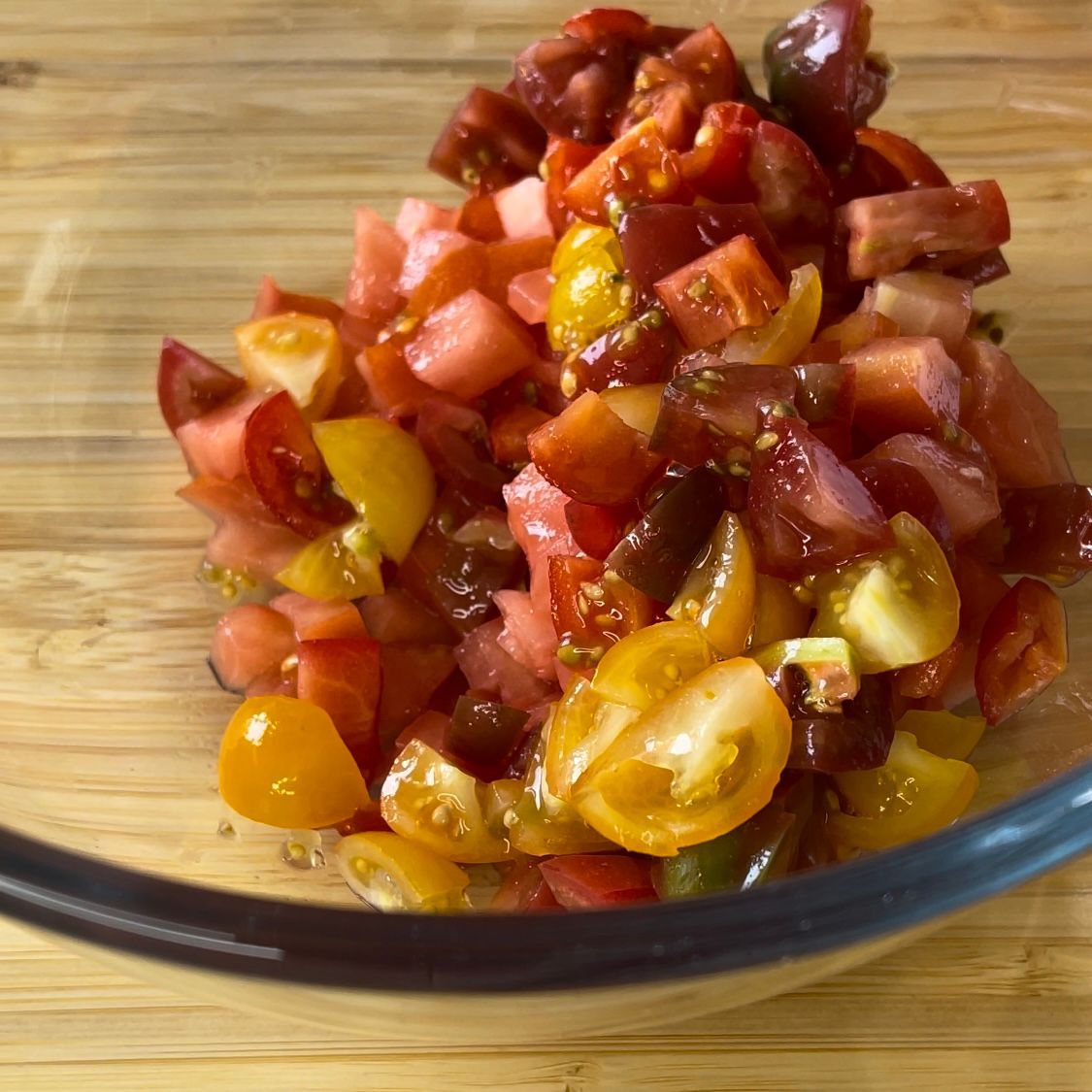 Una ciotola di vetro piena di pomodori e olive su un tavolo di legno.