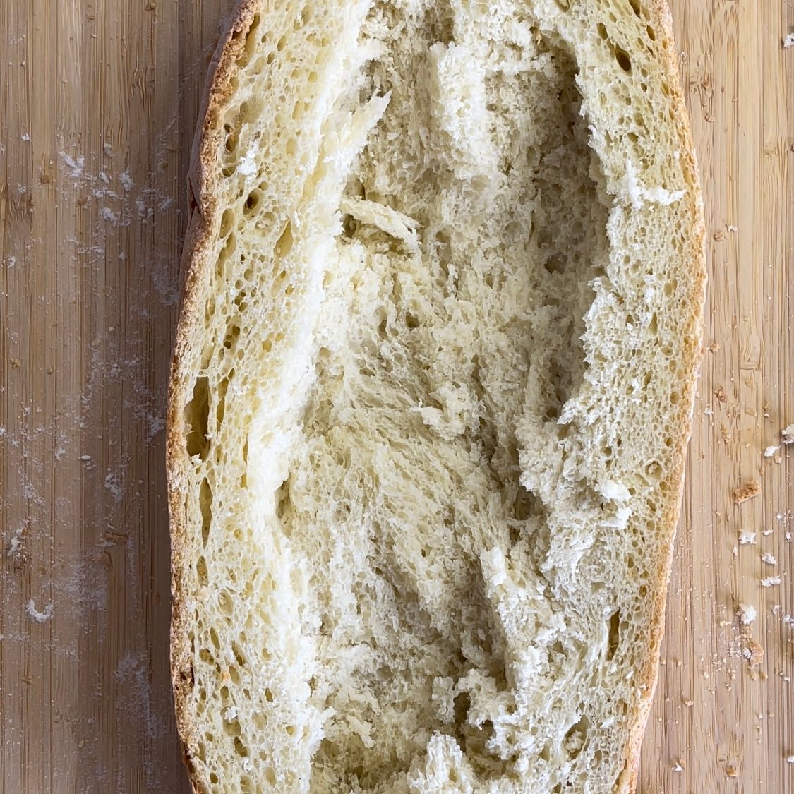 Una pagnotta di pane viene tagliata a metà su un tagliere di legno.