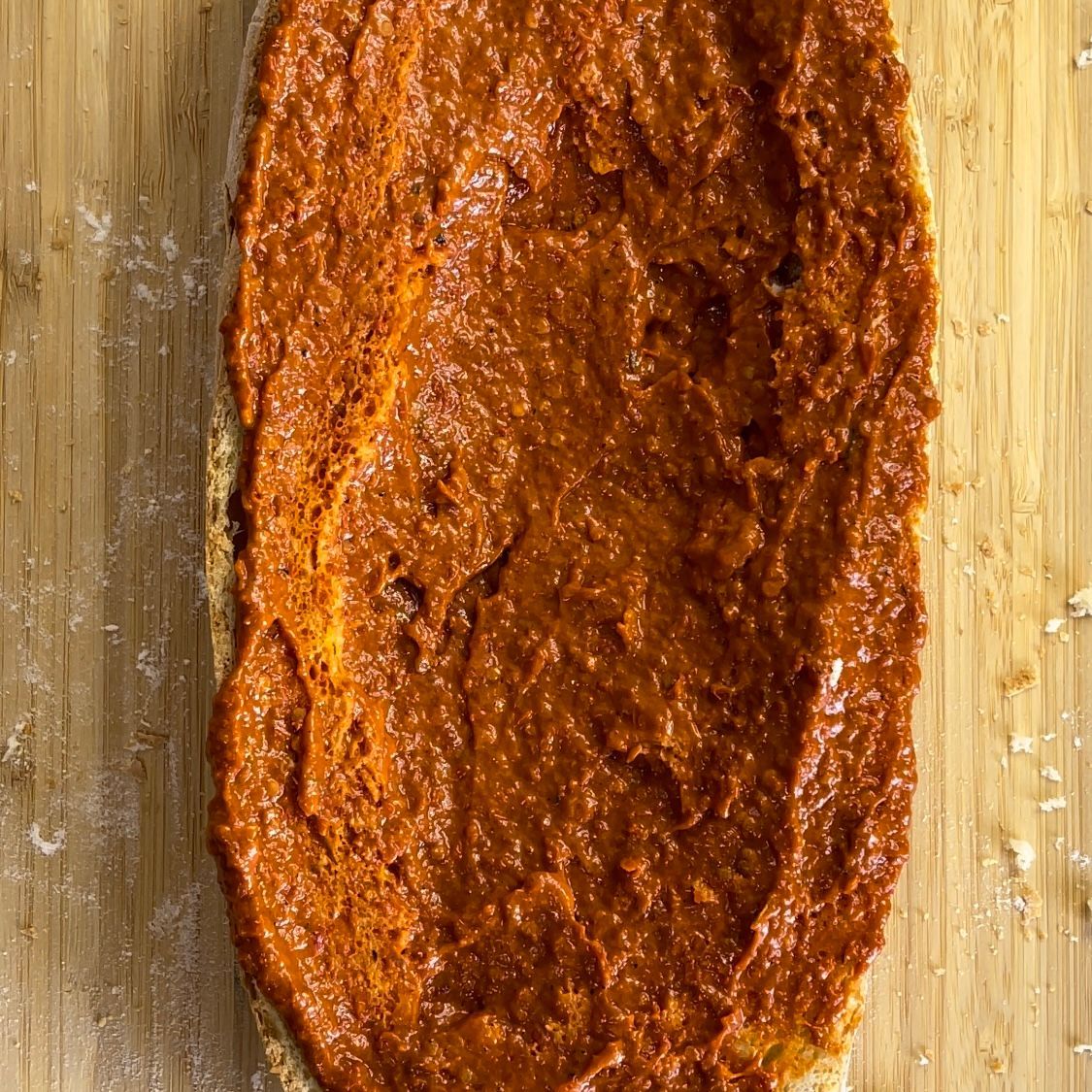 Un pezzo di pane ricoperto di salsa rossa su un tagliere di legno.