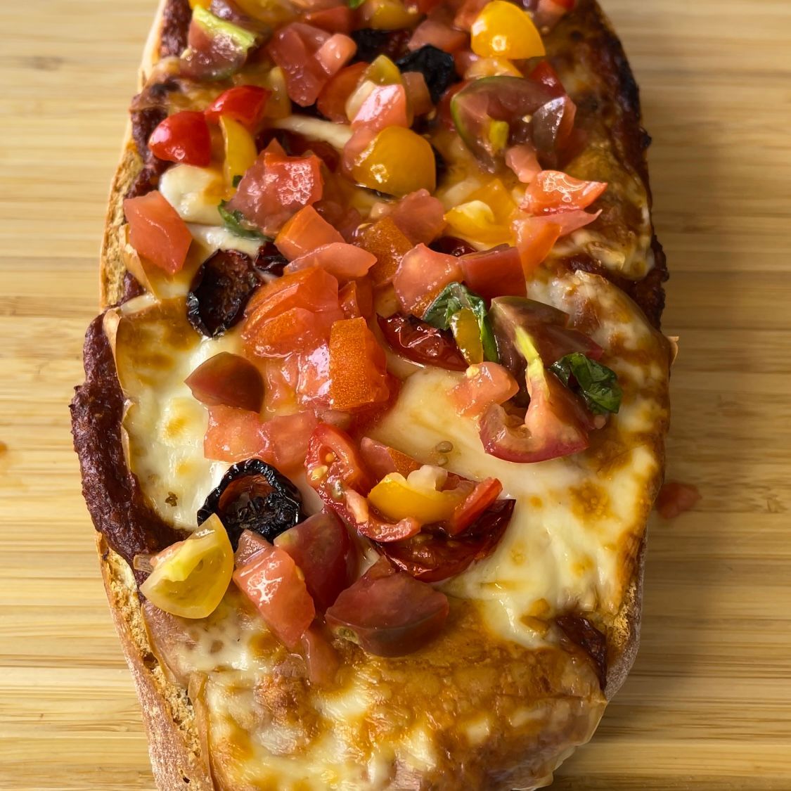 Una pizza con pomodori, olive e formaggio su un tagliere di legno.