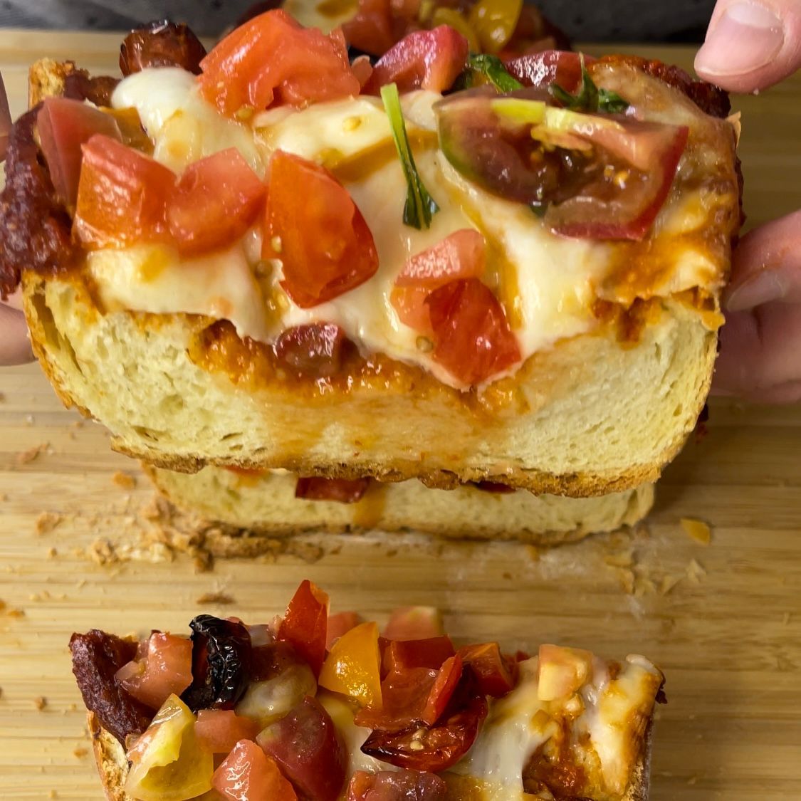 Una persona tiene in mano una fetta di pizza con pomodori e formaggio.