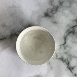 Una ciotola bianca piena d'acqua è appoggiata su una superficie di marmo.