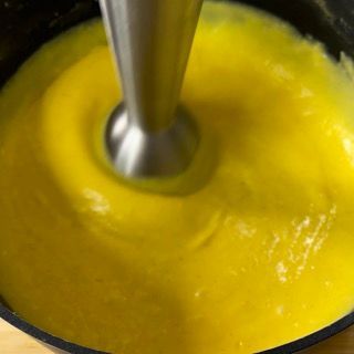 Si sta utilizzando un frullatore per frullare una salsa gialla in una pentola.