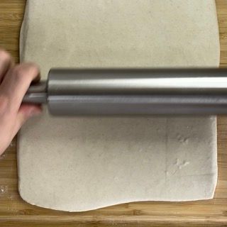 Una persona sta stendendo la pasta con un mattarello su un tagliere di legno.