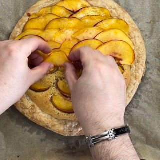 Una persona che indossa un orologio sta mettendo delle pesche su una pizza