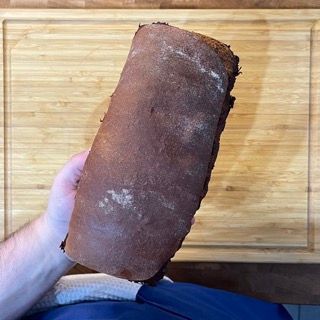 Una persona tiene in mano una pagnotta di pane davanti a un tagliere di legno.