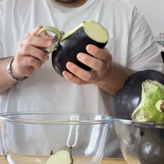 Un uomo con una camicia bianca sta sbucciando una melanzana