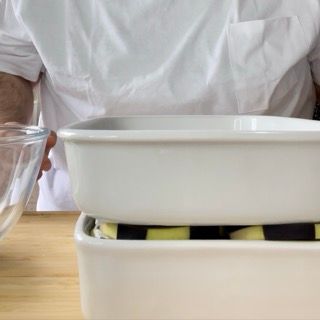 Un uomo con una camicia bianca tiene in mano una ciotola di vetro accanto a due contenitori bianchi