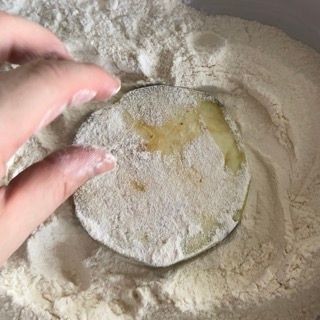 Una persona tiene in mano un pezzo di cibo in una ciotola di farina.