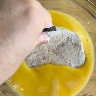 Una persona sta immergendo un pezzo di carne in una ciotola di uova.