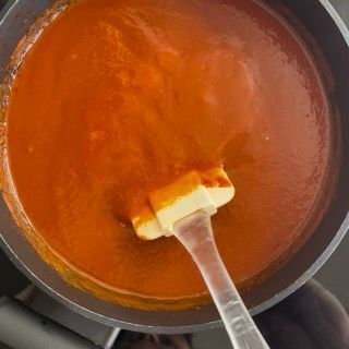 Una padella di salsa di pomodoro con un pezzo di burro su una spatola.