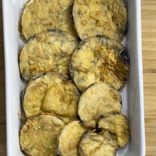 Una teglia bianca piena di fette di melanzane fritte su un tavolo di legno.