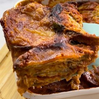 Un pezzo di lasagna viene tolto da una teglia con una spatola.