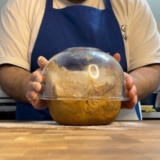 Un uomo con un grembiule tiene una cupola di plastica sopra una ciotola di cibo