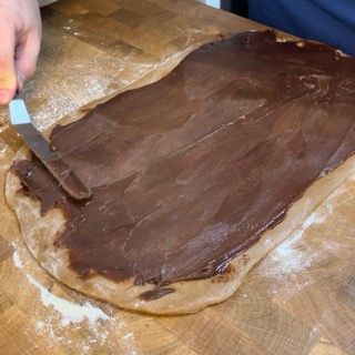 Una persona sta spalmando la salsa al cioccolato su un pezzo di pasta.