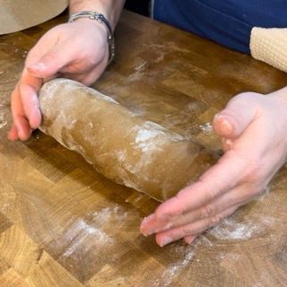 Una persona sta stendendo un pezzo di pasta su un tavolo di legno.