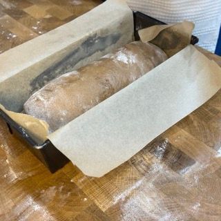 Una pagnotta di pane è avvolta in carta oleata su un tavolo di legno
