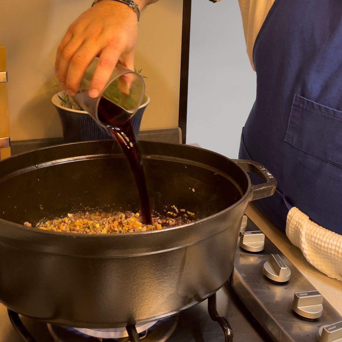 Vino rosso versato nella pentola per sfumare la base del ragù