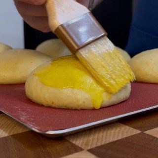 Una persona sta usando un pennello per spalmare la salsa gialla su un panino