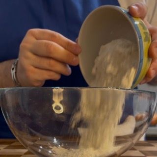 Una persona sta versando la farina in una ciotola di vetro