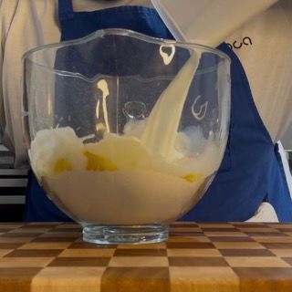 Una persona con un grembiule sta versando qualcosa in una ciotola di vetro