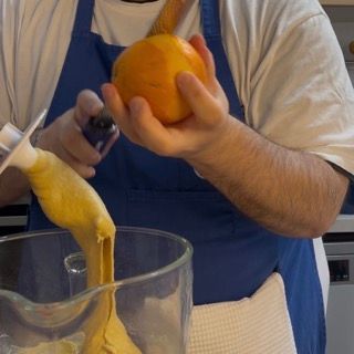 Un uomo con un grembiule tiene in mano un'arancia e la versa in un bicchiere