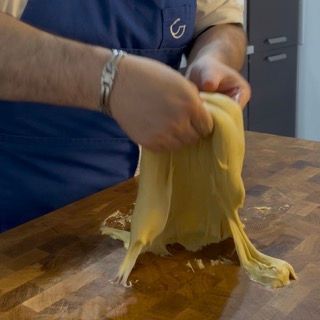 Un uomo con un grembiule blu tiene in mano un pezzo di pasta