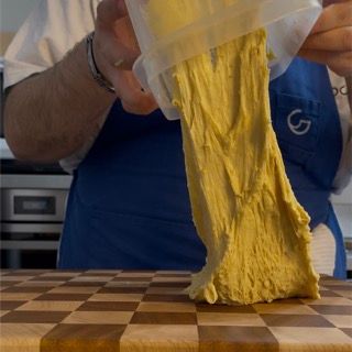 Una persona con un grembiule blu tiene in mano un sacchetto di pasta