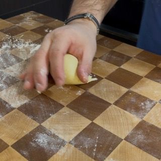 Una persona tiene in mano una palla di pasta su un tagliere a scacchi