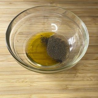 Una ciotola di vetro piena di olio e pepe nero su un tavolo di legno.