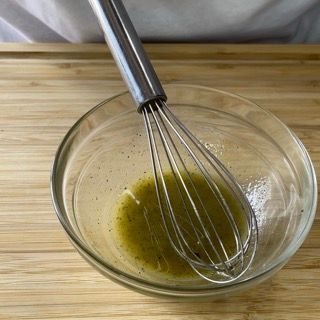 Una frusta è in una ciotola di liquido su un tavolo di legno.