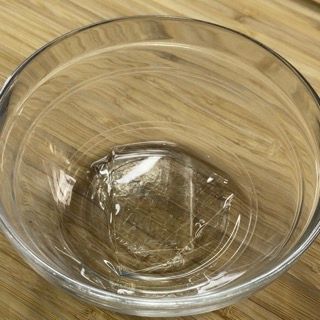 Una ciotola di vetro trasparente è appoggiata su un tavolo di legno.