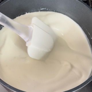 Un cucchiaio bianco mescola un liquido bianco in una padella.