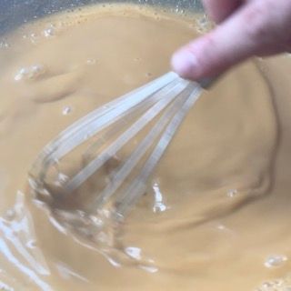 Una persona sta mescolando un liquido marrone con una frusta.