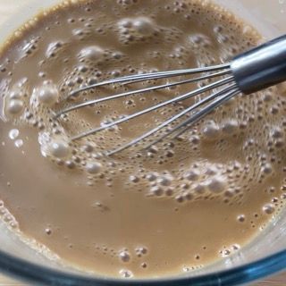 Si usa una frusta per mescolare un liquido marrone in una ciotola di vetro.