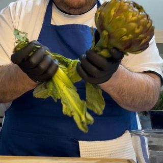 Un uomo con un grembiule blu tiene in mano un carciofo