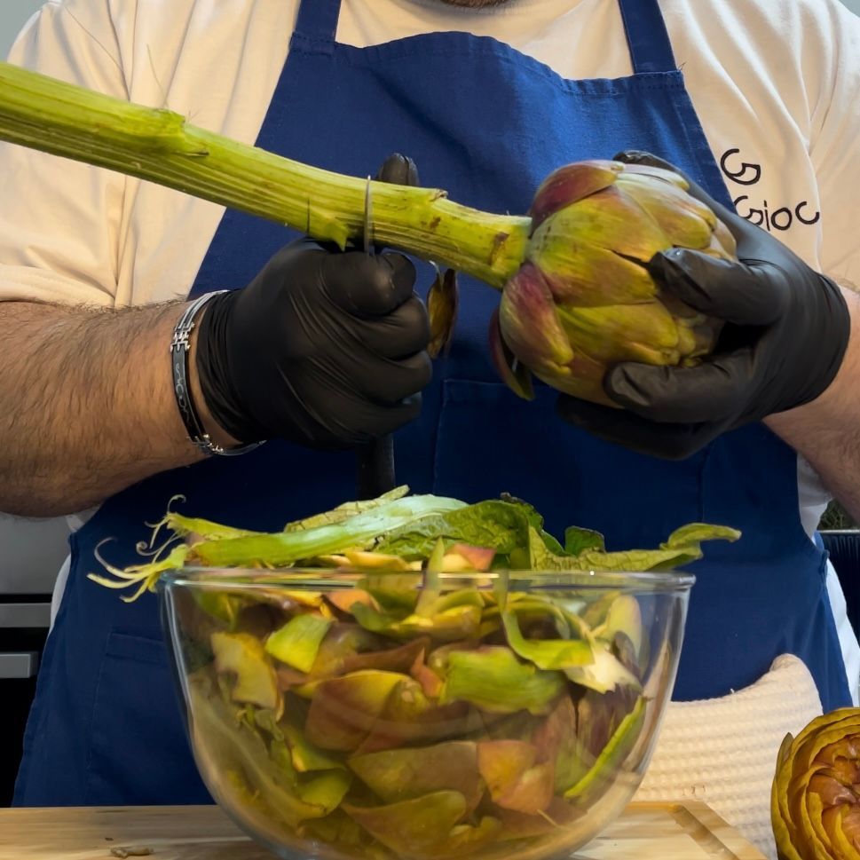 Un uomo che indossa guanti neri sta sbucciando i carciofi
