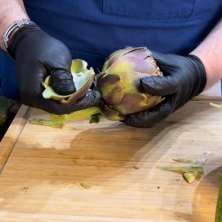 Un uomo che indossa guanti neri sta sbucciando un carciofo su un tagliere