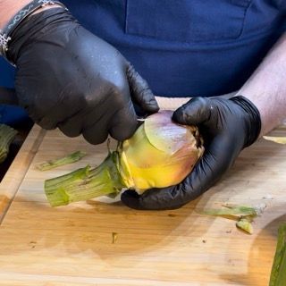 Una persona che indossa guanti neri sta tagliando un carciofo