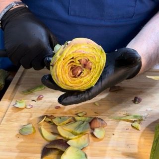 Una persona che indossa guanti neri sta tagliando un carciofo