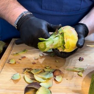 Un uomo che indossa guanti neri sta sbucciando un carciofo su un tagliere