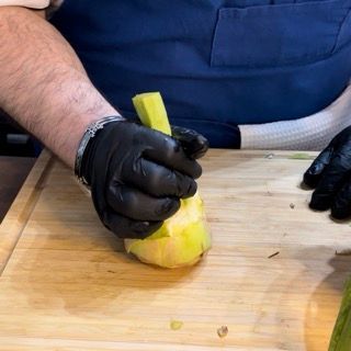 Una persona che indossa guanti neri sta tagliando una verdura verde su un tagliere.