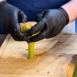 Una persona che indossa guanti neri tiene in mano un pezzo di cibo su un tagliere.